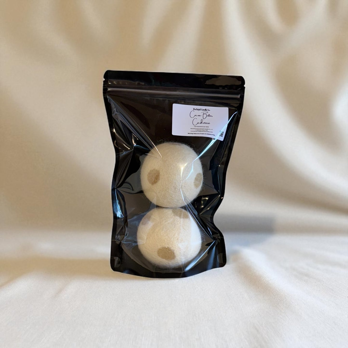 Two white laundry detergent pods in a black packaging bag on a beige fabric background