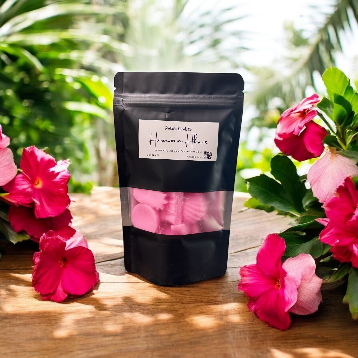Black packaging with pink items on a wooden surface surrounded by pink flowers