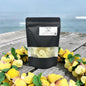 Black packaging with a label on a wooden surface with yellow flowers and water in the background