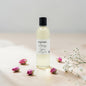 A bottle of Poshlight Candles Co. Aromatic Gaze lye soap with a black cap and white label, styled on a beige surface with pink rose buds and white baby's breath flowers.