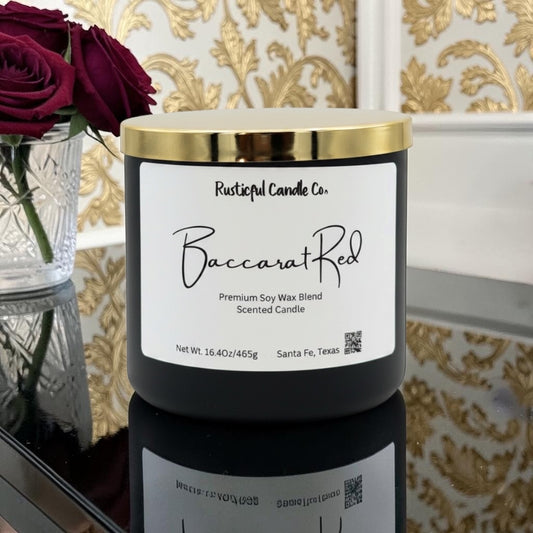 Candle labeled 'Baccarat Red' from Rusticful Candle Co. with gold lid on a reflective surface.
