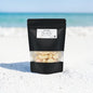 Black packaging of white chocolate chips on a sandy beach with blue sky.