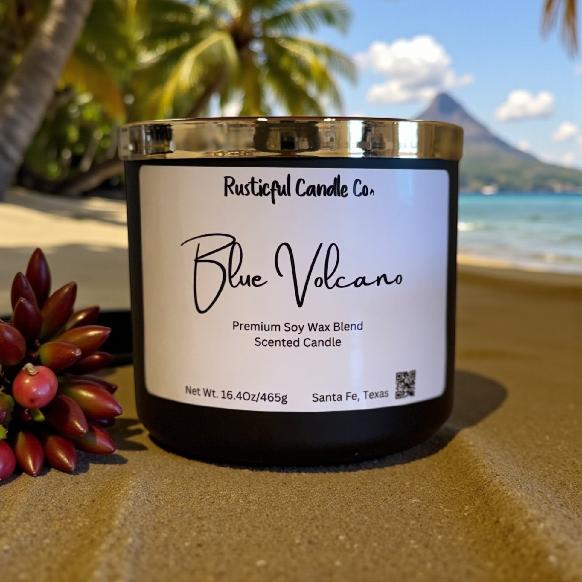 Candle labeled 'Blue Volcano' from Rusticful Candle Co. on a beach with palm trees and mountains in the background.
