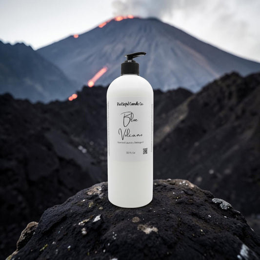A large white pump bottle labeled 'Portugal Candles Co. Blue Villare' stands on a dark volcanic rock with a blurred volcano and lava in the background.