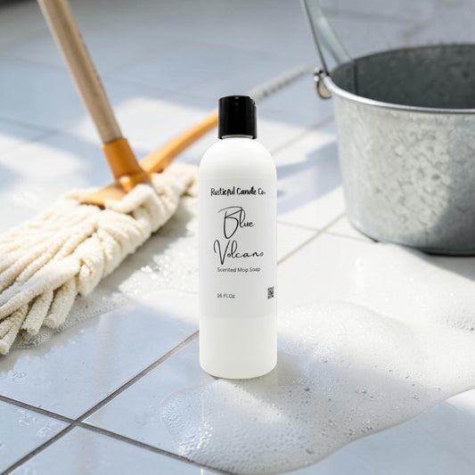 A bottle of Butterfly Candles Co. Blue Vicar Steamless Soap Spray stands on a tiled floor with soapy water and a mop nearby, alongside a galvanized bucket.
