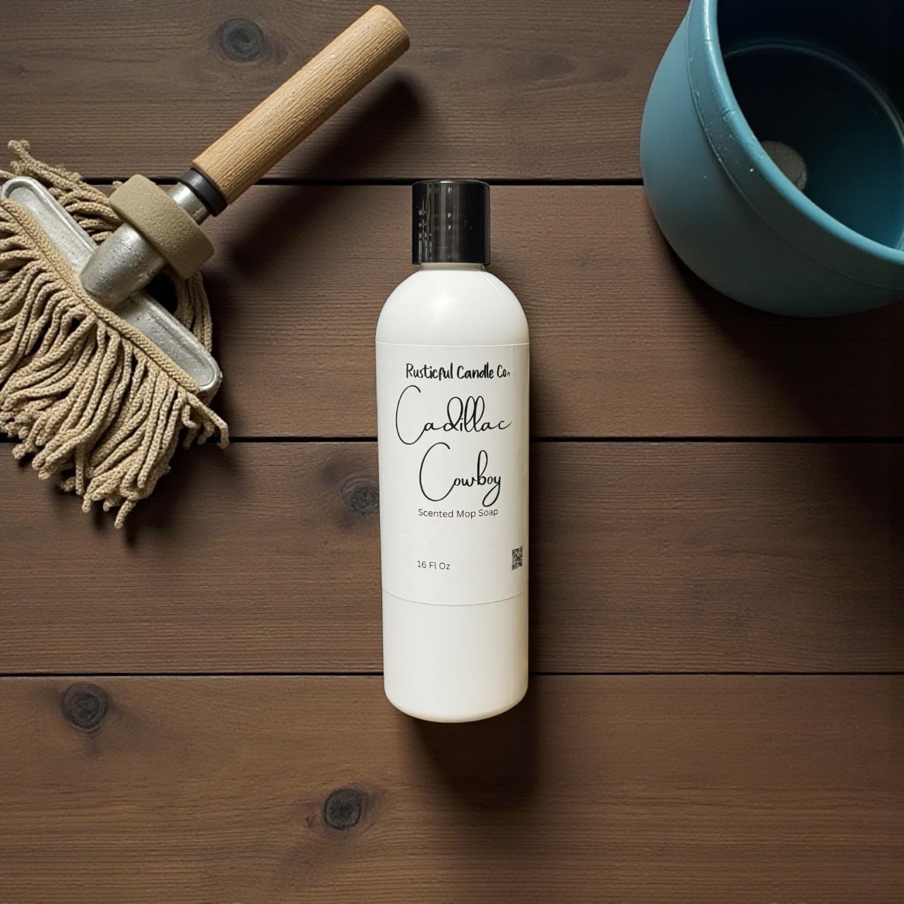 Bottle of 'Cadillac Cowboy' scented mop cleaner on a wooden surface with a mop and blue container.