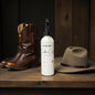Bottle of leather care product with cowboy boots and hat on a wooden surface