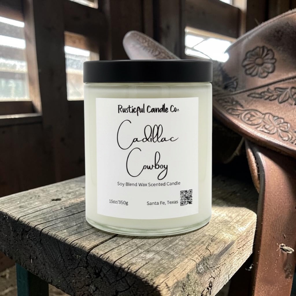Candle labeled 'Cadillac Cowboy' by Rusticful Candle Co. on a wooden surface with leather goods in the background.