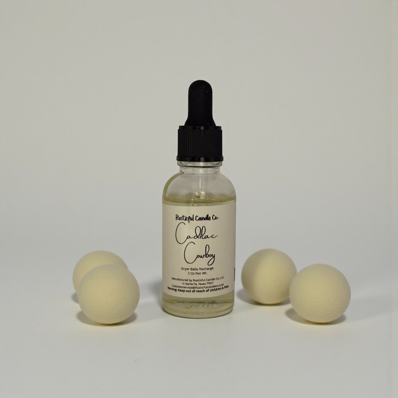Bottle of Cadillac Cowboy dryer balls refresher with dryer balls on a light gray background
