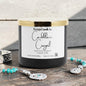 Black candle with a white label on a wooden surface, surrounded by jewelry.