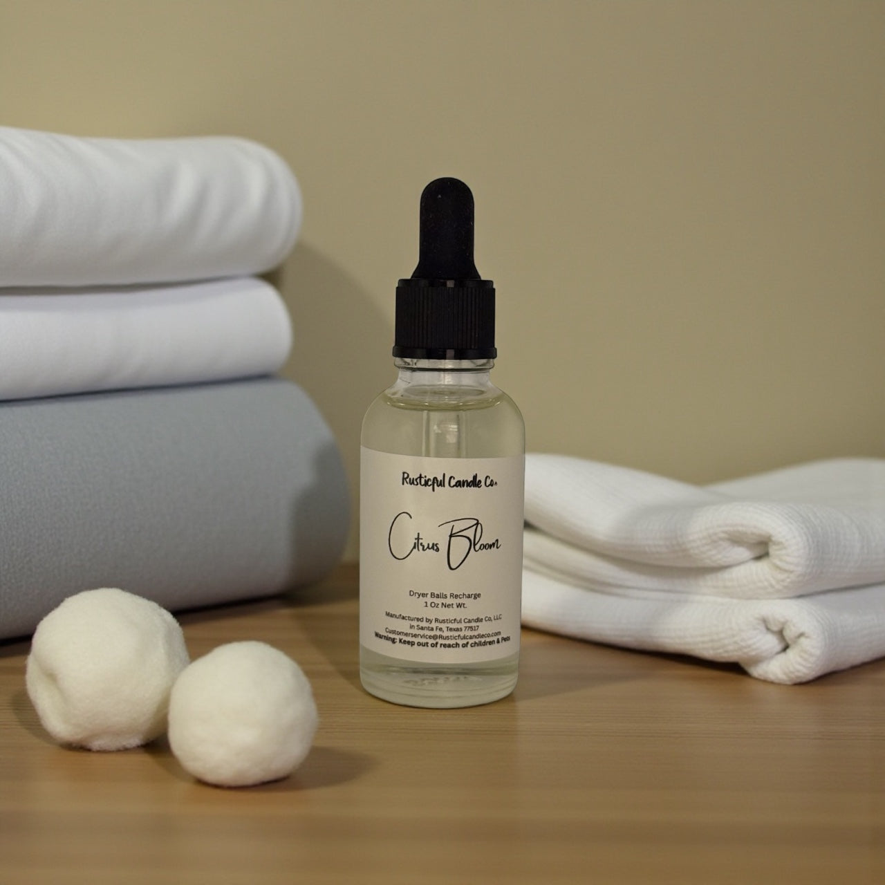 Bottle of 'Crisp Bloom' with dryer balls and folded towels on a wooden surface.