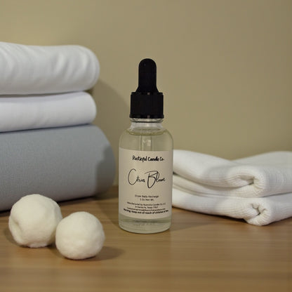 Bottle of 'Crisp Bloom' with dryer balls and folded towels on a wooden surface.