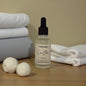 Bottle of 'Crisp Bloom' with dryer balls and folded towels on a wooden surface.