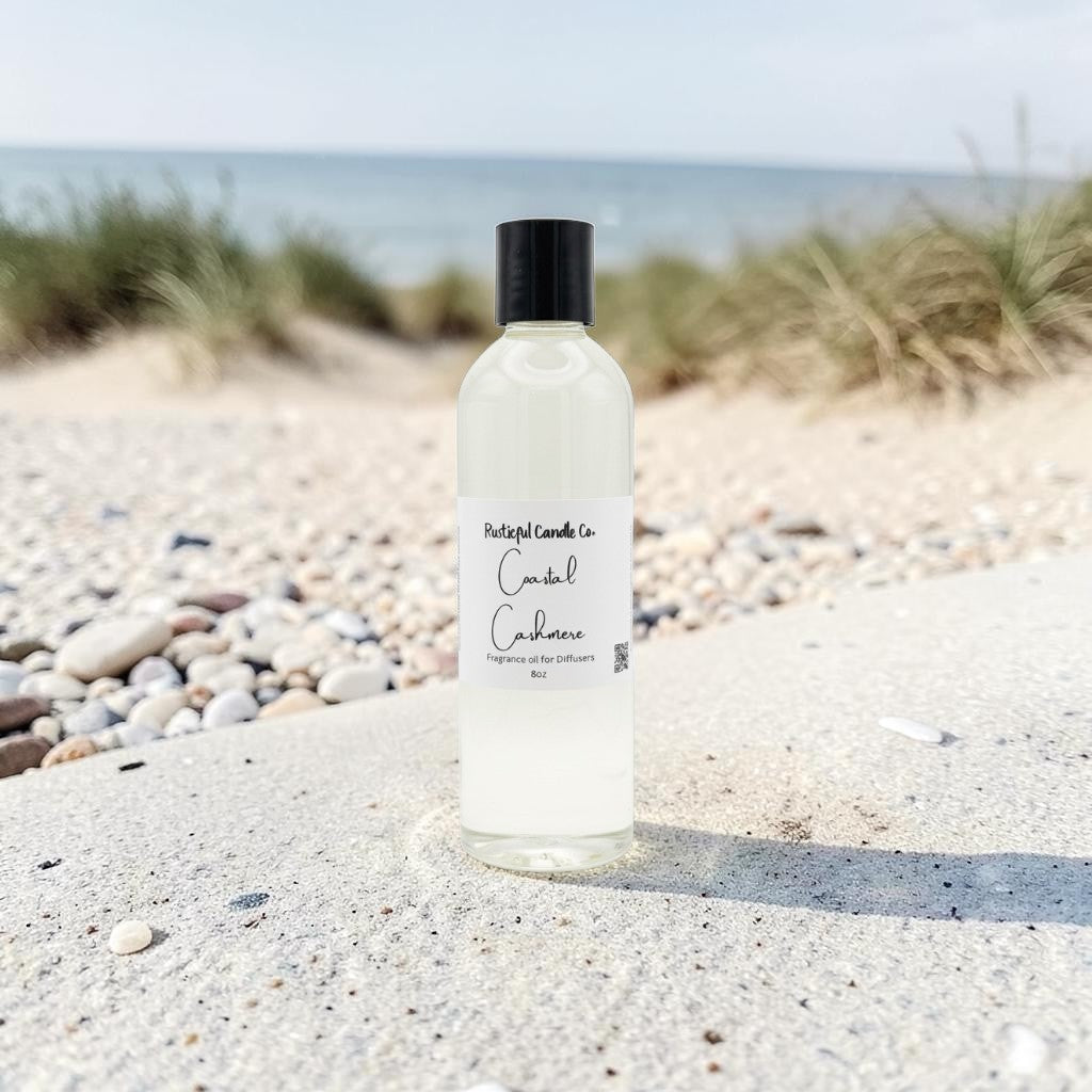 A bottle of daylight candles 'Candle Cushion' scented oil diffuser and candle, placed on a sandy beach with pebbles and dune grass in the background.