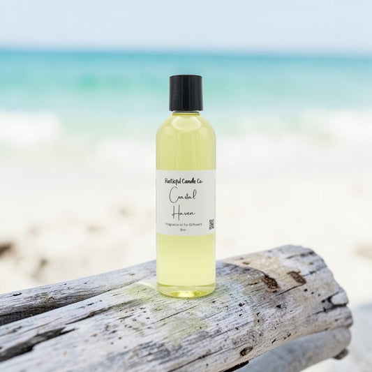 A bottle of Natural Candles Co. Candle Hair fragrance oil sits on a weathered piece of driftwood with a blurred beach and ocean background.