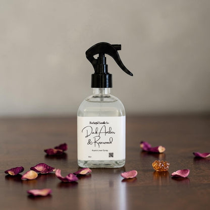 Clear spray bottle with black nozzle on a wooden surface with dried flowers and amber gemstones.