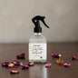 Clear spray bottle with black nozzle on a wooden surface with dried flowers and amber gemstones.