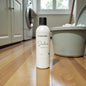 Bottle of 'Beautiful Candle Co' product on a wooden floor with laundry equipment in the background