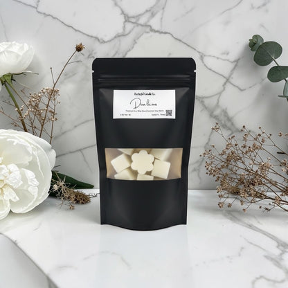 Black packaging with a clear window showing white cubes, placed on a marble surface with flowers.