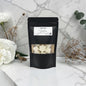 Black packaging with a clear window showing white cubes, placed on a marble surface with flowers.