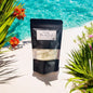 Black package with a label on a white surface with flowers and water in the background