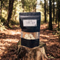 Black candle packaging on a wooden stump in a forest setting