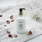 Hand lotion bottle labeled 'Gypsy Blush' on a textured surface with flowers and petals.