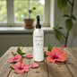 White bottle with black cap on a wooden table with pink flowers and green leaves.