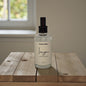 Bottle of 'Imagine' scented body mist on a wooden surface with a neutral background