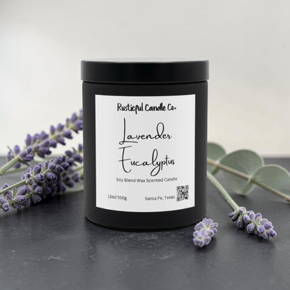 A black jar candle with a white label reading 'Lavender Eucalyptus' by Rusticful Candle Co., styled on a dark surface with lavender sprigs and eucalyptus leaves around it.