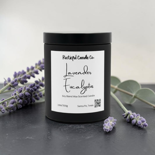 A black jar candle with a white label reading 'Lavender Eucalyptus' by Rusticful Candle Co., styled on a dark surface with lavender sprigs and eucalyptus leaves around it.