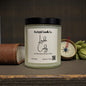 Candle with a label on a wooden surface, surrounded by decorative items.