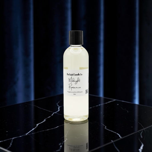 A clear bottle of Mayi Rose essential oil by Portugal Candle Co. with a black cap, standing on a black marble surface against a dark blue curtain background.