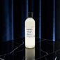 A clear bottle of Mayi Rose essential oil by Portugal Candle Co. with a black cap, standing on a black marble surface against a dark blue curtain background.