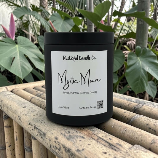 Black candle labeled 'Mystic Man' from Rusticful Candle Co. on a wooden surface with plants in the background