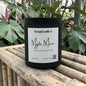 Black candle labeled 'Mystic Man' from Rusticful Candle Co. on a wooden surface with plants in the background