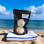 Packaged bath bombs on a towel with a beach background
