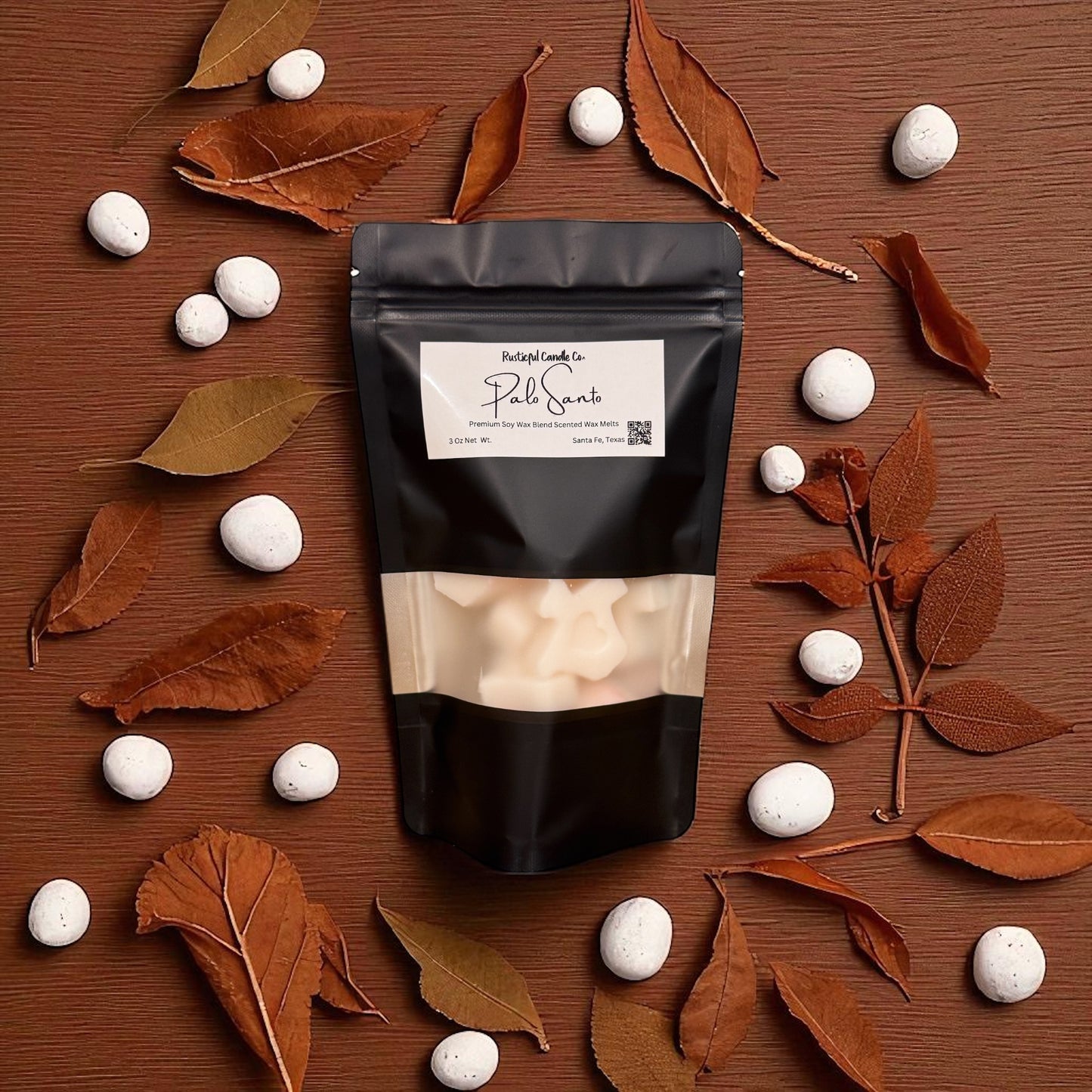 Black packaging with a label on a wooden surface with white stones and brown leaves.
