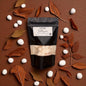 Black packaging with a label on a wooden surface with white stones and brown leaves.