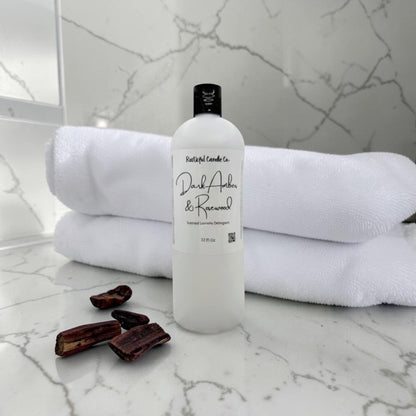 Bottle of 'Dark Amber & Renewed' soap on a marble surface with towels and dates.