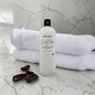 Bottle of 'Dark Amber & Renewed' soap on a marble surface with towels and dates.