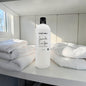 White bottle of laundry detergent with towels on a table in a bright room