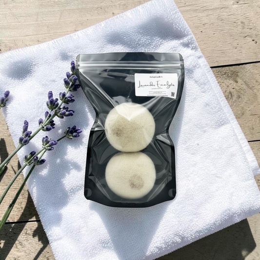 Two white dryer balls in a clear plastic bag on a white towel with lavender flowers beside it.