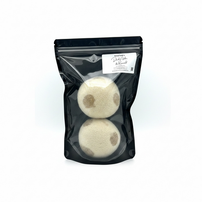 Two white bath bombs with brown spots in a clear plastic bag on a white background