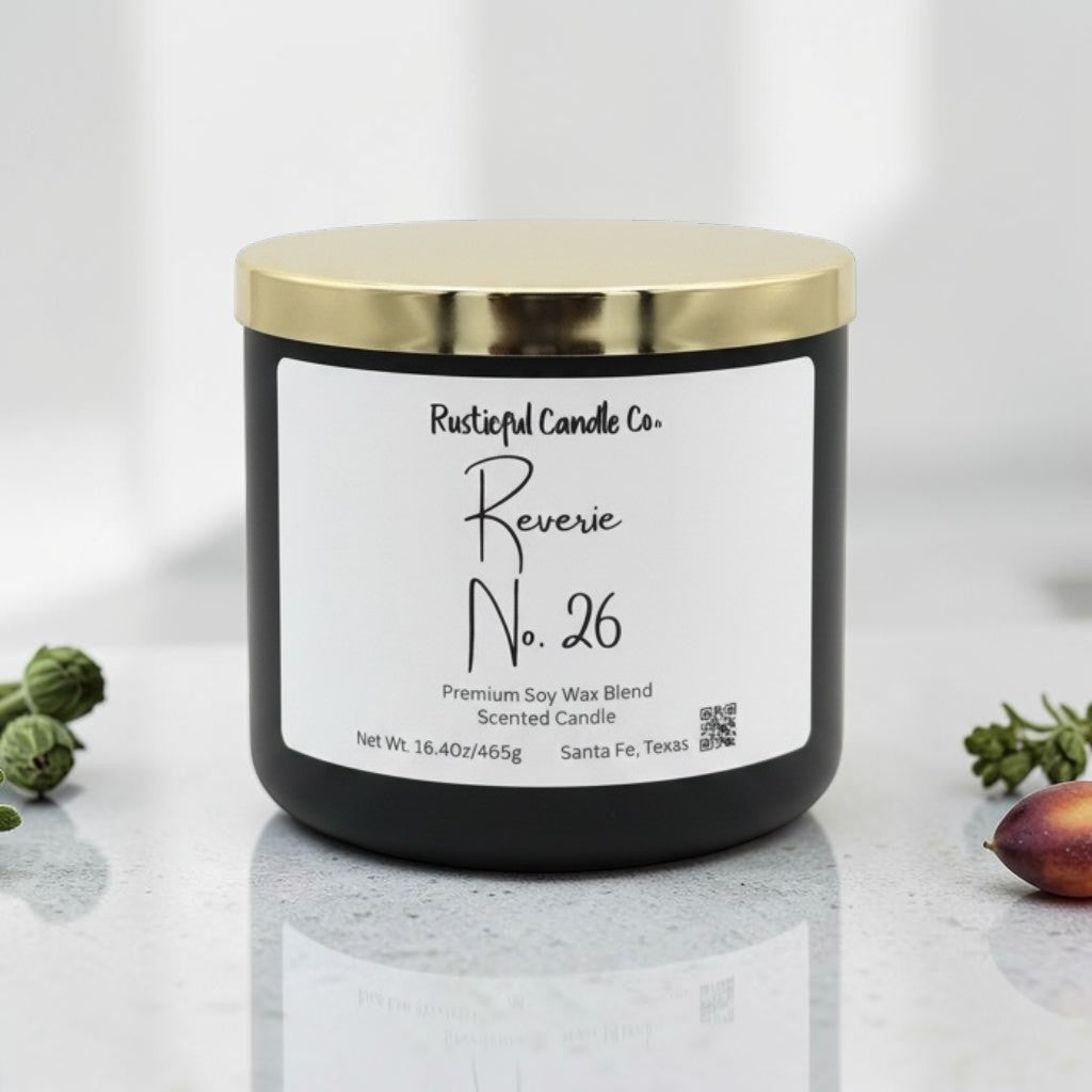 A black jar candle with a shiny gold lid and a white label reading 'Rustical Candle Co. Reverie No.