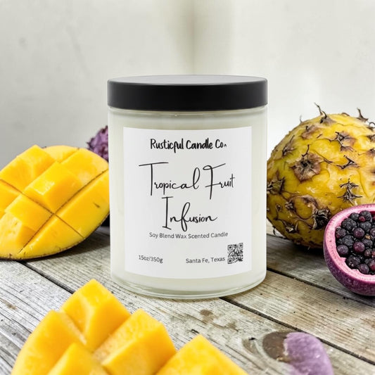 Candle labeled 'Tropical Fruit Infusion' with a pineapple, mango, and blackberry on a wooden surface.