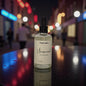 Bottle of 'Unsupervised' scented body mist on a reflective surface with a blurred city street background