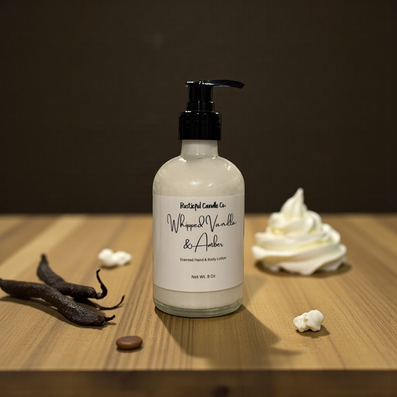 Bottle of whipped vanilla and amber scented product on a wooden surface with vanilla beans and cream.