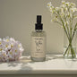 Bottle of 'White Sun' scented body mist with flowers on a surface