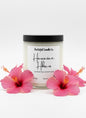 Candle with 'Hawaiian Hibiscus' label surrounded by pink flowers on a white background